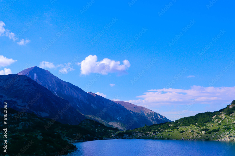 Beautiful mountains lake with a reflection of the high green mountains peaks, on the blue sky background. Amazing Mountain hiking paradise landscape with a lake, no people. Beautiful mountains lake with a reflection of the high green mountains peaks, on the blue sky background. Amazing Mountain hiking paradise landscape with a lake, no people.
