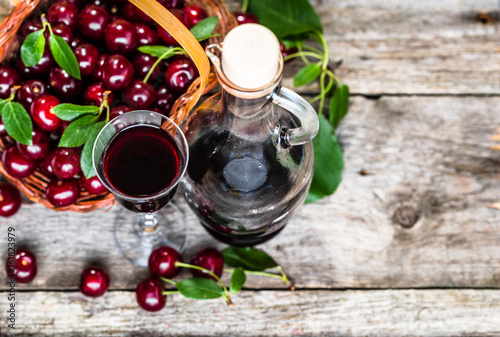 Glass of alcohol tincture made from cherry fruits, liquor in a bottle on rustic background
