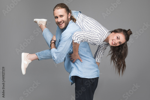 Canvas Print Cheerful young man carrying happy young woman and smiling at camera