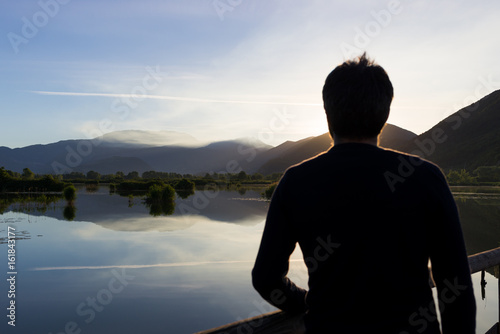 Man looking at beautiful sunrise sunset reflection at Iseo lake in Italy in summer