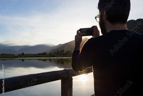 Man took a picture with a smartphone of beautiful sunrise sunset reflection at Iseo lake in Italy in summer