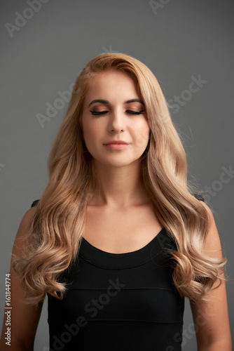 Waist-up portrait of beautiful blonde-haired woman with evening makeup posing with her eyes closed