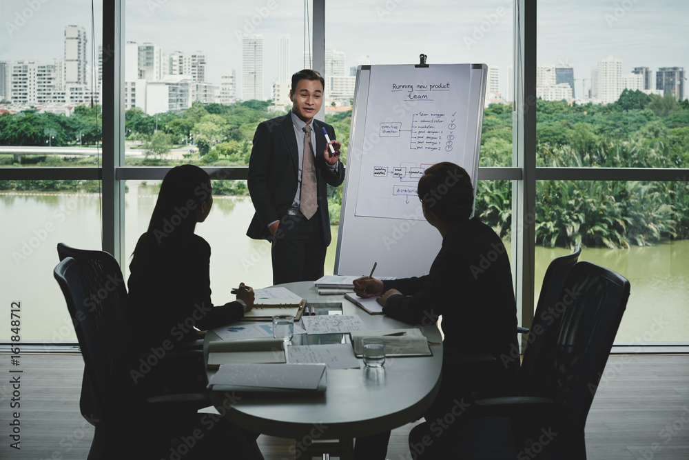 Vietnamese white collar worker presenting his start-up project to potential investors while having meeting in modern boardroom with panoramic windows