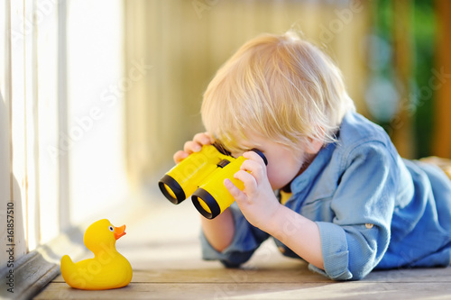 Foto Cute little boy playing with rubber duck and plastic binoculars outdoors