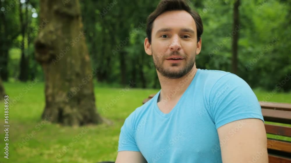 Young fit man stretching legs while sitting on the bench in the park. Man showing thumbs up. Close up Young fit man stretching legs while sitting on the bench in the park. Man showing thumbs up. Close up