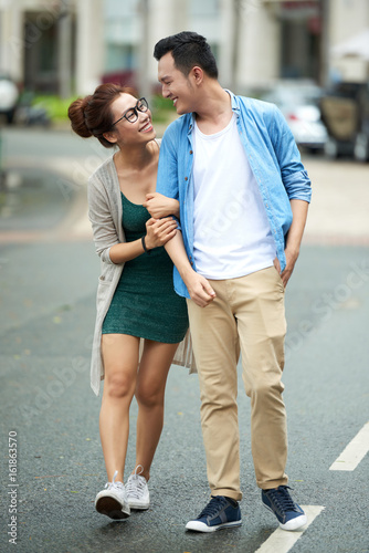 Portrait of young man and woman walking close together in street of big city and smiling looking at each other with love