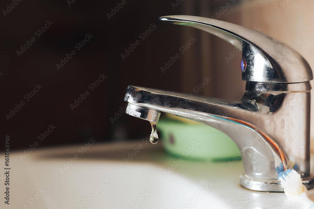 Metal faucet with falling drops of water close-up