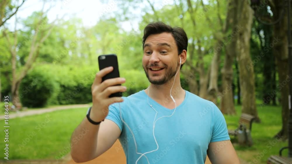 Attractive young fit man video chatting during his morning run in the park. Video call with friends on smart phone. Close up