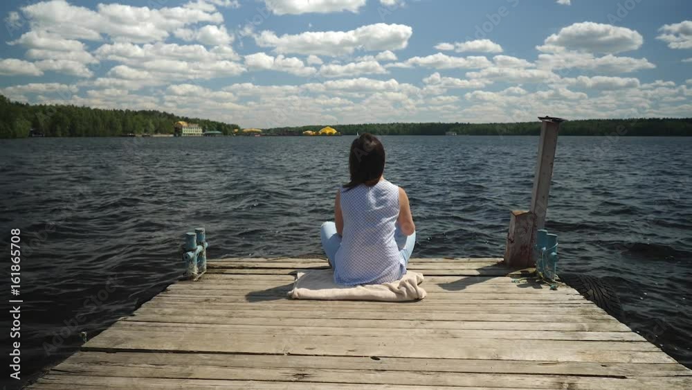 Young woman sits in lotus pose on old wooden pier throws up her hands. Young woman sits in lotus pose on old wooden pier throws up her hands.