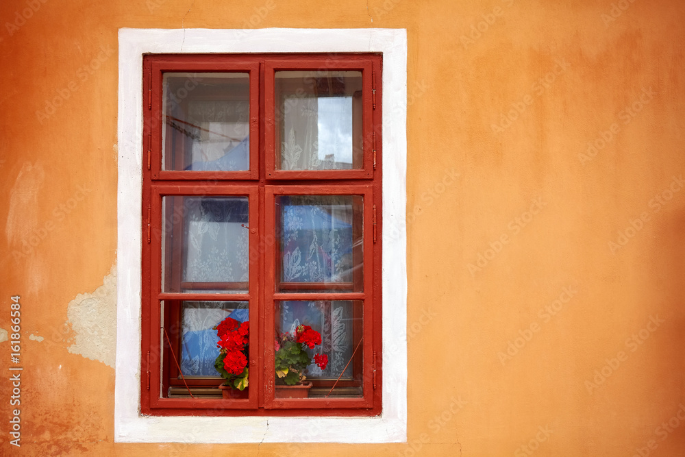 An old window with red flowers in orange wall, copy space on the side.