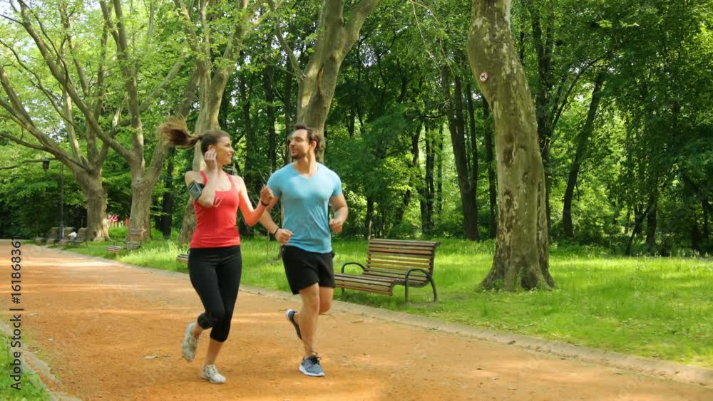 Young man and woman running together in the park. Beautiful couple having morning run, jog. Slow Motion. Young man and woman running together in the park. Beautiful couple having morning run, jog. Slow Motion.