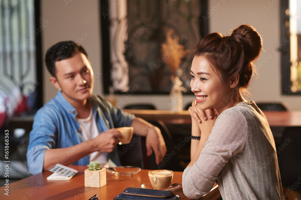 Portrait of beautiful Asian woman enjoying evening in cafe with man watching her in background