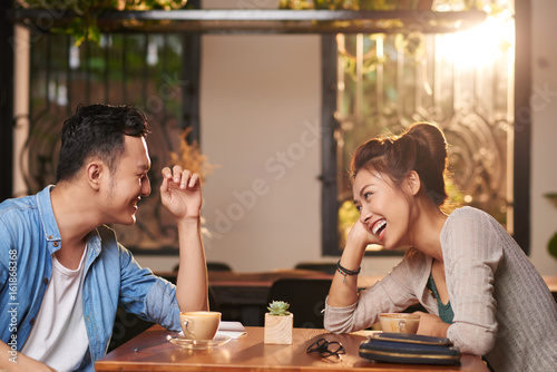 Side view portrait of laughing Asian couple enjoying date in cafe photo