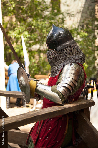 Middle ages period costume at knight tournament. Medieval historical reenactment - a man wearing metal helmet and armor suit, holding a sword and a shield photo