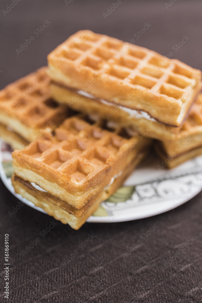 Sweet Viennese waffles with white filling lie on a saucer on a dark brown background, vertical frame Sweet Viennese waffles with white filling lie on a saucer on a dark brown background, vertical frame
