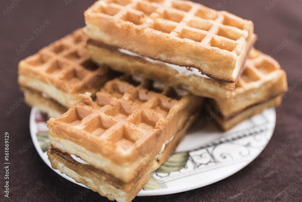 Delicious Viennese waffles with a filling lie on a saucer on a dark brown background, close-up Delicious Viennese waffles with a filling lie on a saucer on a dark brown background, close-up