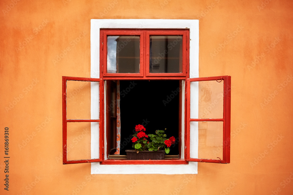 Opened old red window with flowers in orange wall