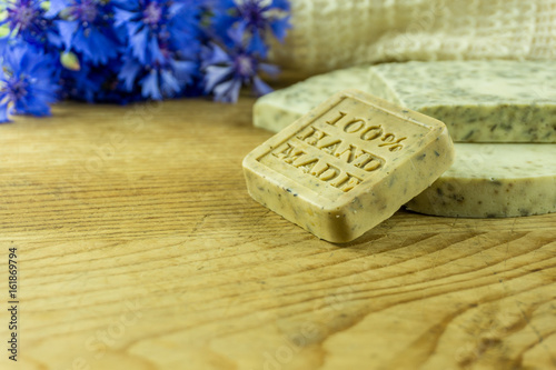 Handmade soap on a rustic wooden board with cornflowers and accessories.