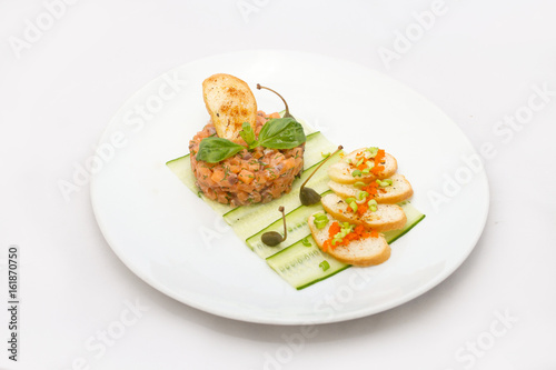 Salmon tartare on a white plate with green leaves