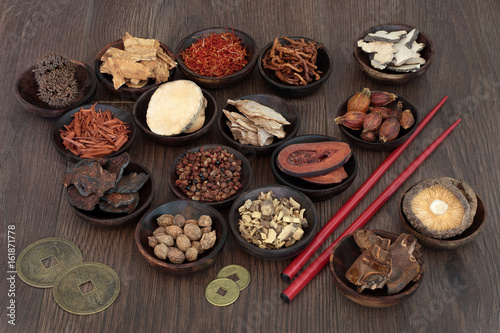 Chinese herbal medicine selection in wooden bowls with feng shui coins and chopsticks on oak background. photo