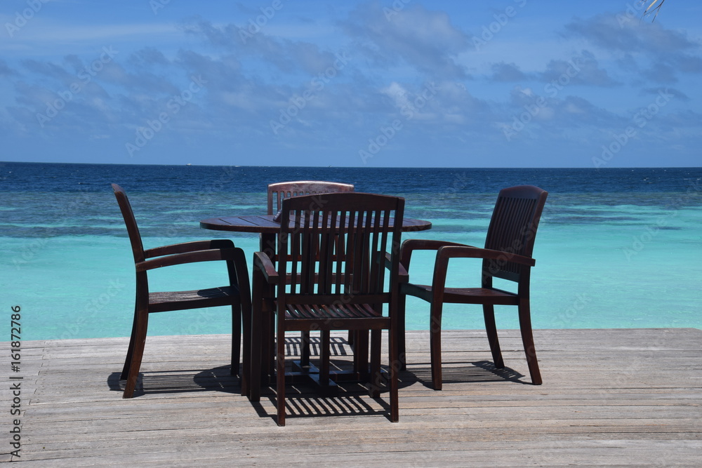 Stühle und Tische auf einem maledivischen Sonnendeck mit schöner türkisfarbener Lagune und blauem Himmel