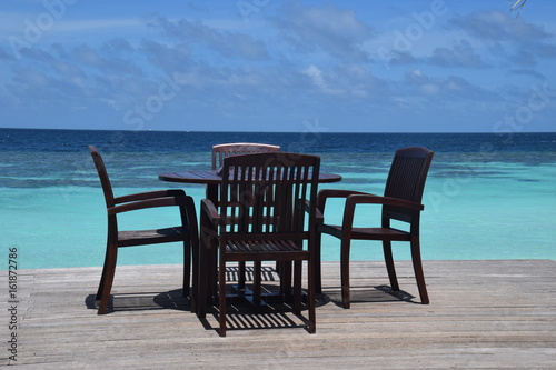 Stühle und Tische auf einem maledivischen Sonnendeck mit schöner türkisfarbener Lagune und blauem Himmel