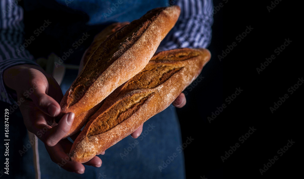 Baker's hands hold fresh bread over dark background