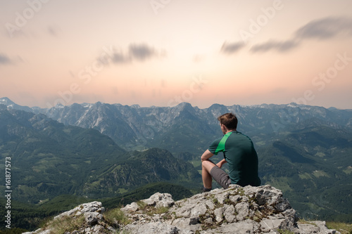 Junger Wanderer macht Pause auf einem Gipfel bei Sonnenuntergang
