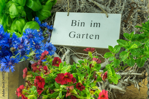 Herbs, flowers and green leaves with a sign in the garden in German