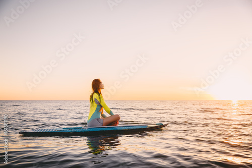 Stand up paddle boarding on a quiet sea with warm sunset colors. Young woman is relaxing on ocean © artifirsov