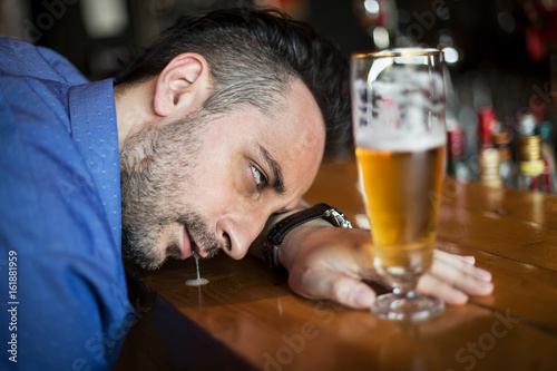 A drunk bearded man holding a glass of beer in his hand and sleeping in the bar
