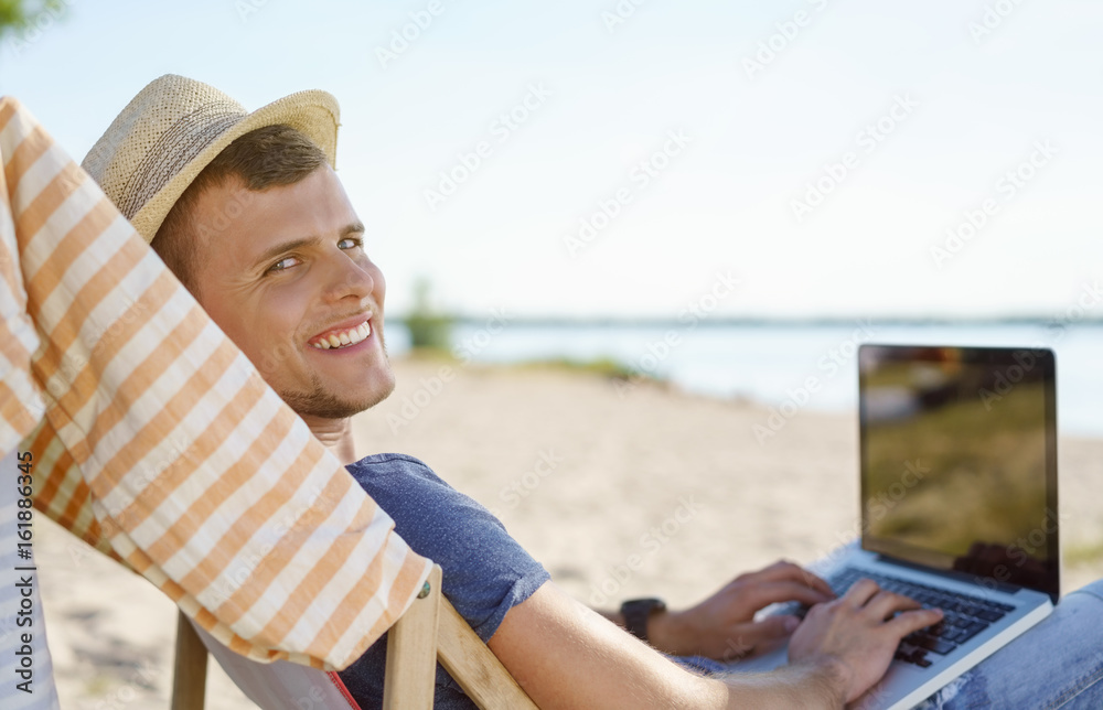 Attractive young man relaxing at the beach with laptop