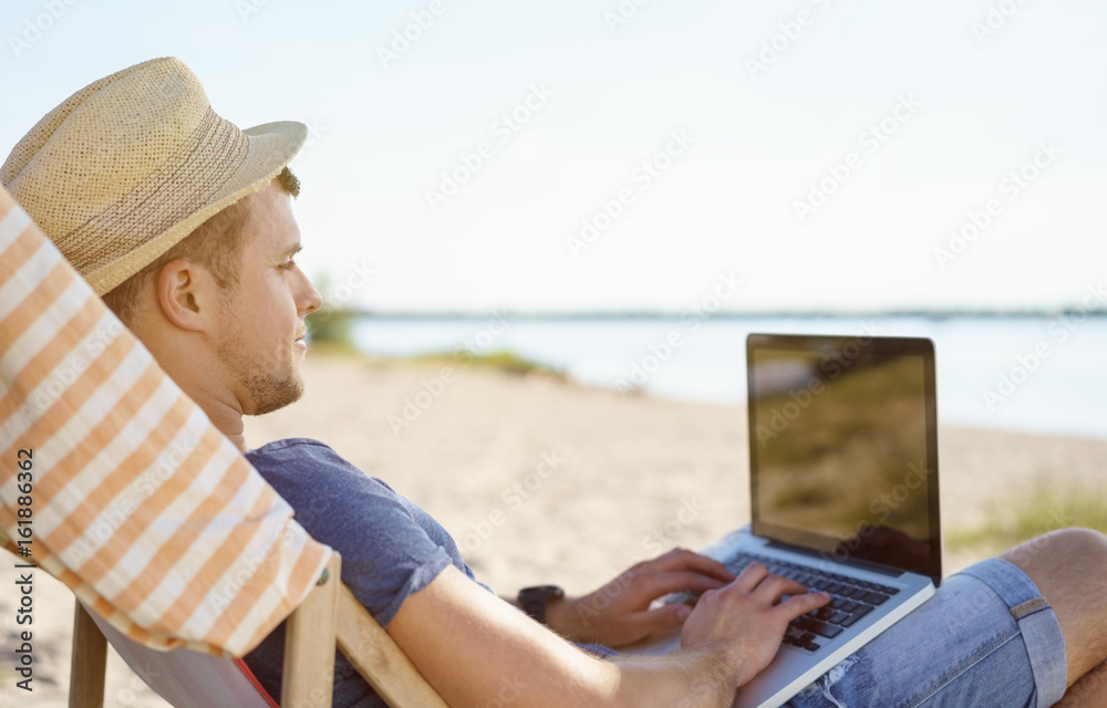 Trendy young man using a laptop at the beach