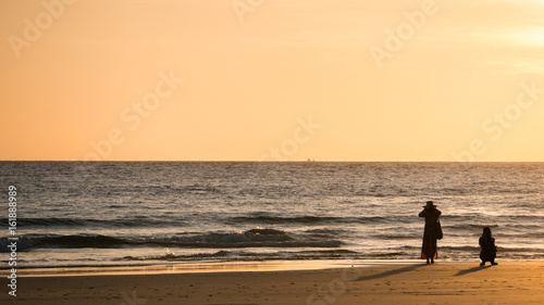 silhouette woman take photo on beach at sunset time.
