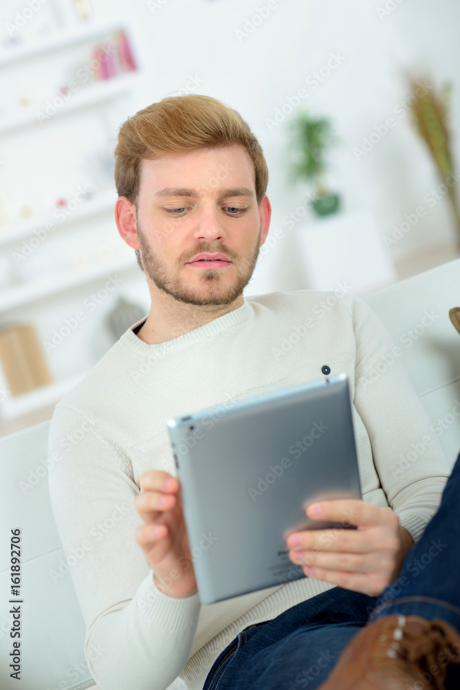 man sitting in sofa using electronic tablet man sitting in sofa using electronic tablet