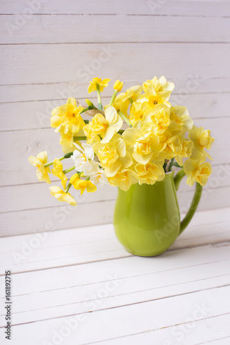 Fototapeta Naklejka Na Ścianę i Meble -  Bright yellow spring daffodils or narcissus flowers in pitcher on white  wooden background.