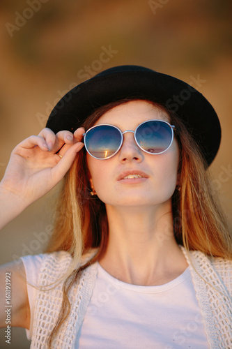 Portrait of young pretty woman wearing hat and sunglasses outdoor on sunset