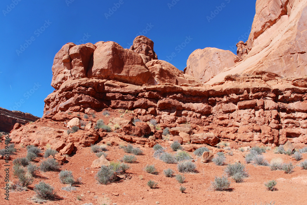Amazing Utah landscape with red sandstones in Arches National Park, Moab, Utah, USA. Nature red sandstone sculptures with sparse green bushes on a foreground against bright blue sky.Nature background. Amazing Utah landscape with red sandstones in Arches National Park, Moab, Utah, USA. Nature red sandstone sculptures with sparse green bushes on a foreground against bright blue sky.Nature background.