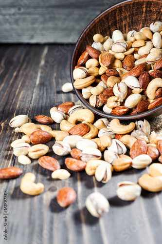 Mixed nuts spilling out of bowl on wooden table. Macro still-life with shallow dof photo