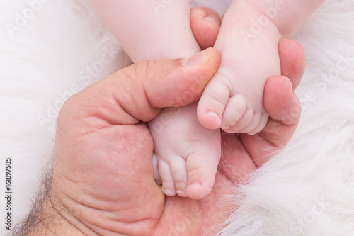 Baby feet on his father hands in soft white blanket 