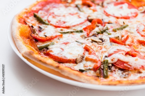 Pizza with tomato, mushrooms, bell peppers on a white plate on a light background