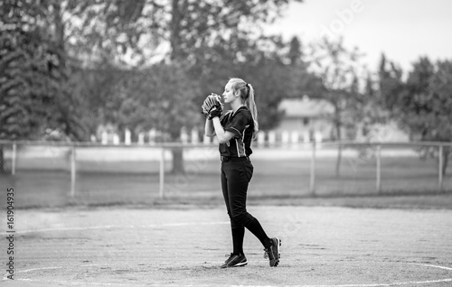 Photography A teenage girl in fast ball pitching stance on the pitchers mound in uniform in