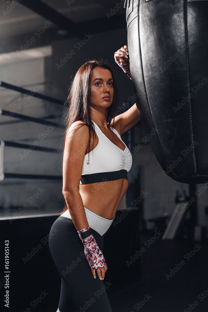 Concentrated woman doing a fitness boxing workout with a punching bag. Young woman boxing workout in sport gym.