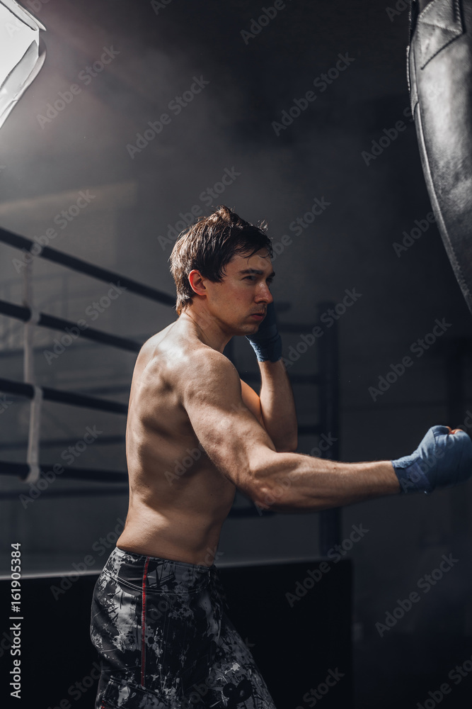 Young sportsman at boxing workout with a punching bag. The concept of a healthy lifestyle.