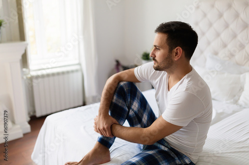 Sad man sitting on bed thinking about problems