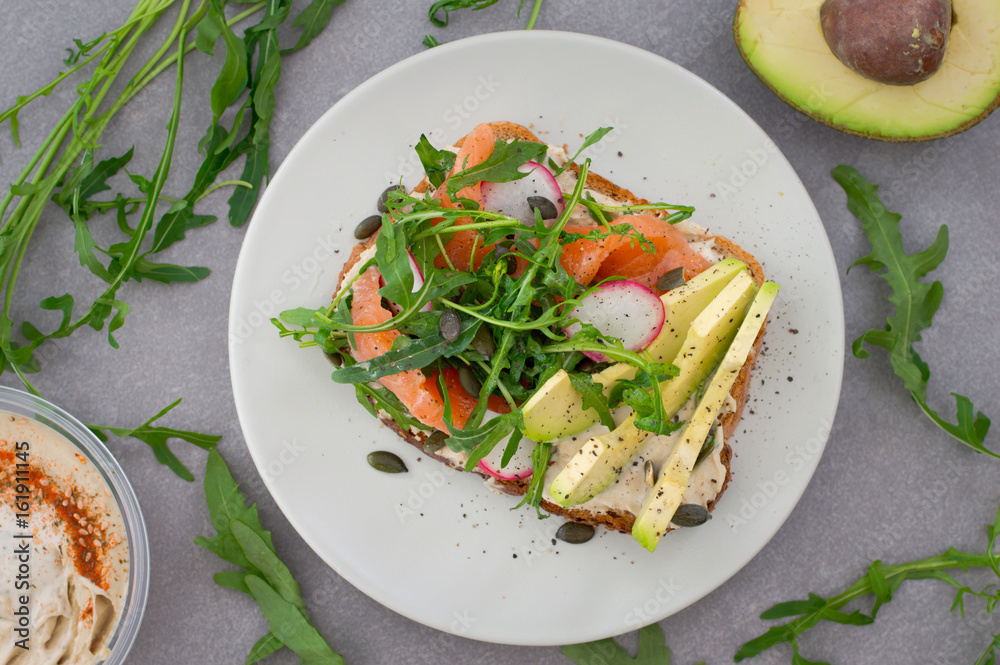 Homemade sandwich with avocado, salmon, arugula and humus. Rustic style. Gray stone background. Close-up. Top view Homemade sandwich with avocado, salmon, arugula and humus. Rustic style. Gray stone background. Close-up. Top view