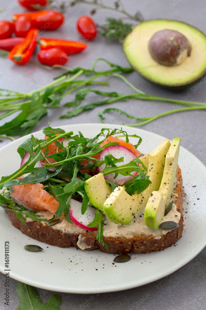 Homemade sandwich with avocado, salmon, arugula and humus. Rustic style. Gray stone background. Close-up. Top view