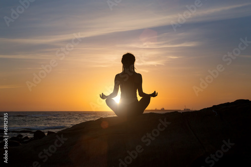 Silhouette young woman practicing yoga on ocean beach at sunset