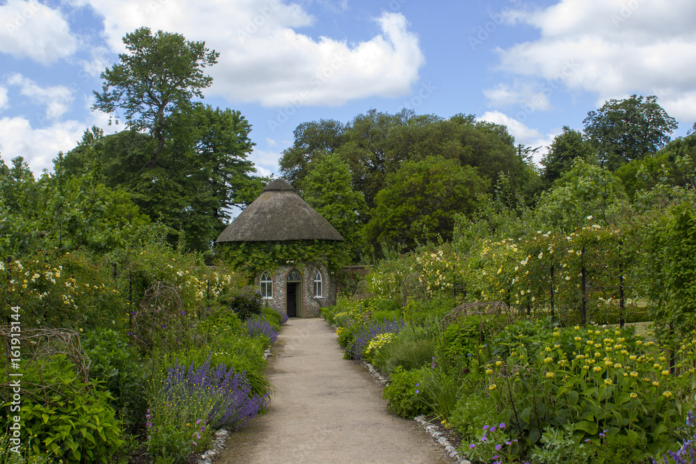 The 19th Century thatched round house surrounded by beautiful flower beds and gravel paths in the walled garden at West Dean gardens in Hampshire, England The 19th Century thatched round house surrounded by beautiful flower beds and gravel paths in the walled garden at West Dean gardens in Hampshire, England