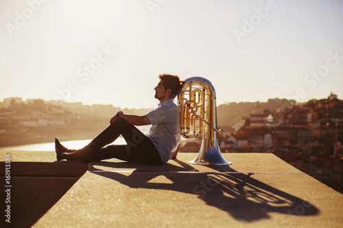 Street musician sitting with tuba outdoor at sunset. Europe city background photo